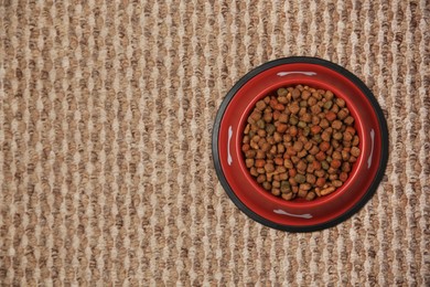 Photo of Dry dog food in feeding bowl on soft carpet, top view. Space for text