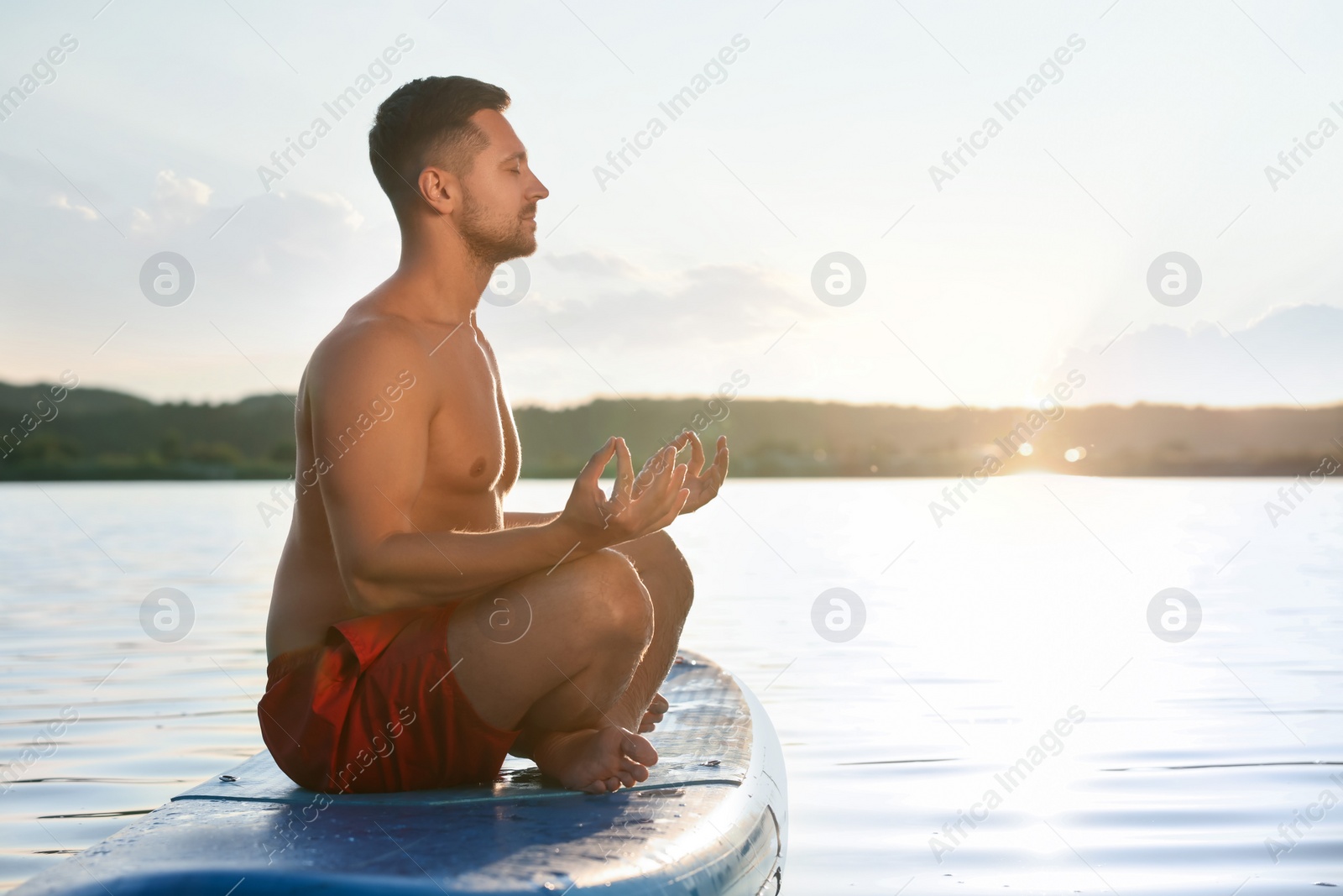 Photo of Man meditating on SUP board on river at sunset