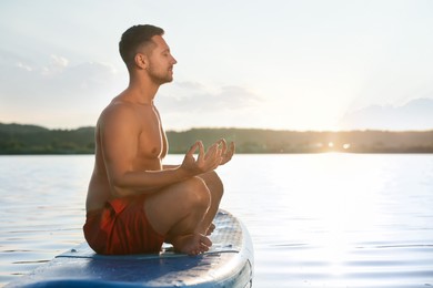 Photo of Man meditating on SUP board on river at sunset