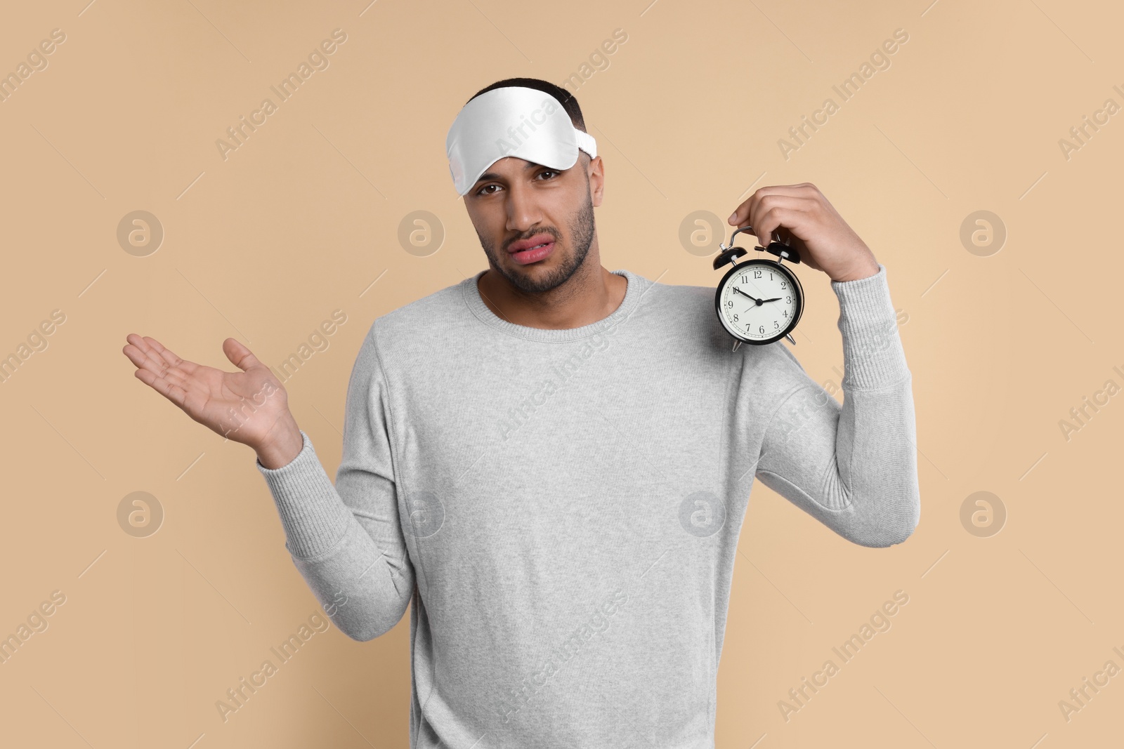 Photo of Tired man with sleep mask and alarm clock on beige background. Insomnia problem