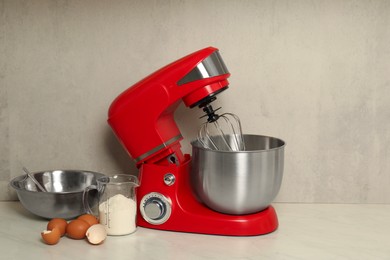 Photo of Modern red stand mixer, eggs, container with flour and bowl on white marble table. Space for text