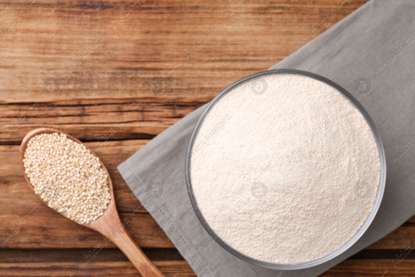 Photo of Quinoa flour in ceramic bowl and spoon with seeds on wooden table, flat lay