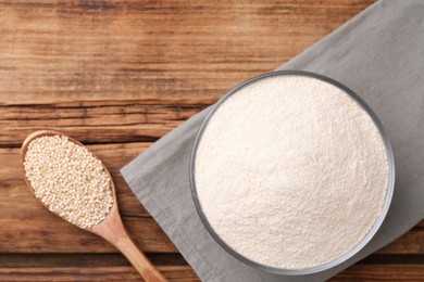 Photo of Quinoa flour in ceramic bowl and spoon with seeds on wooden table, flat lay