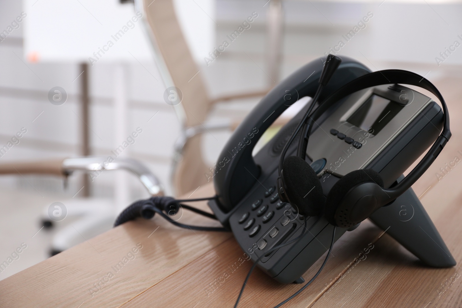 Photo of Desktop telephone and headset on wooden table in office, space for text. Hotline service