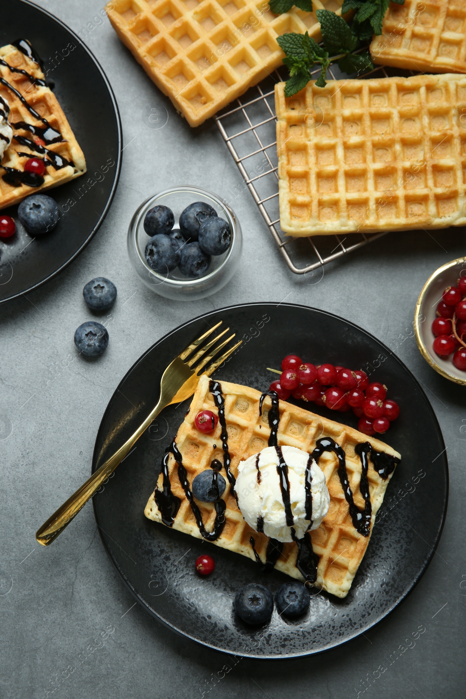 Photo of Delicious Belgian waffles with ice cream, berries and chocolate sauce on grey table, flat lay