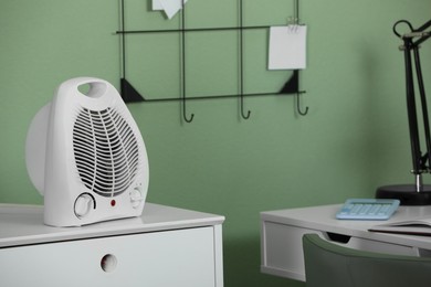 Photo of Modern electric fan heater on chest of drawers indoors. Space for text
