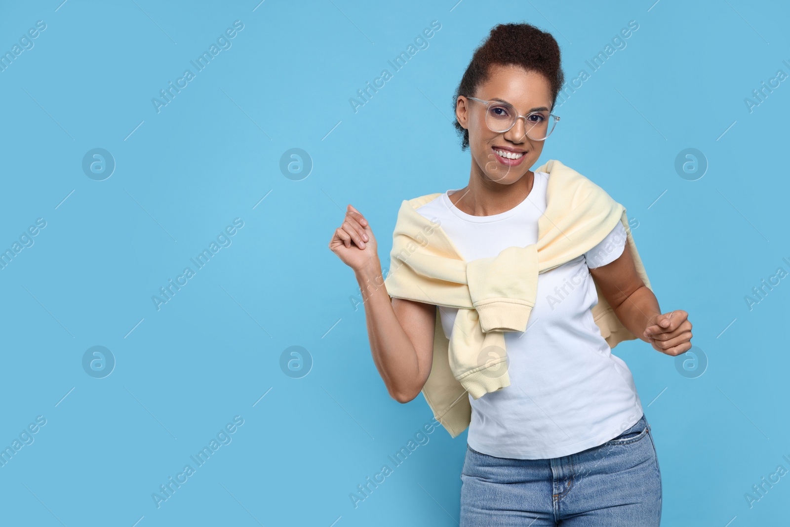 Photo of Happy young woman in stylish eyeglasses dancing on light blue background. Space for text