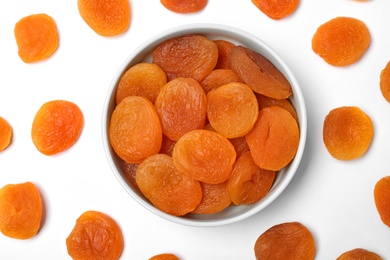 Photo of Flat lay composition with bowl of dried apricots on white background. Healthy fruit
