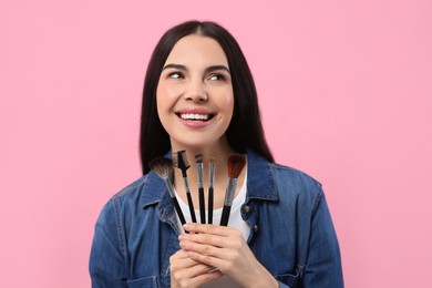 Photo of Happy woman with different makeup brushes on pink background