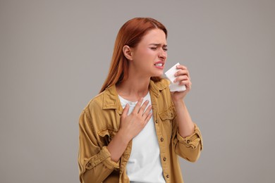 Photo of Suffering from allergy. Young woman with tissue sneezing on grey background