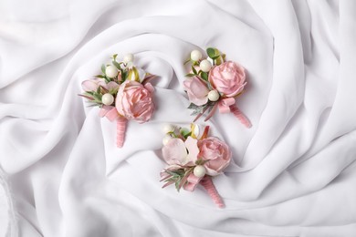 Photo of Stylish pink boutonnieres on white silk, flat lay
