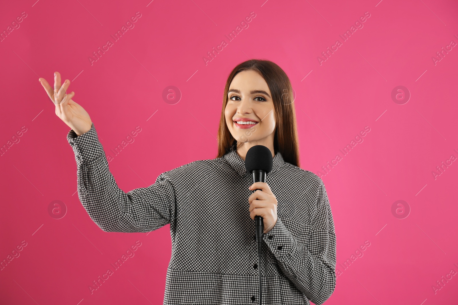 Photo of Young female journalist with microphone on pink background