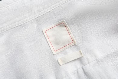 Photo of Blank clothing labels on white shirt, top view