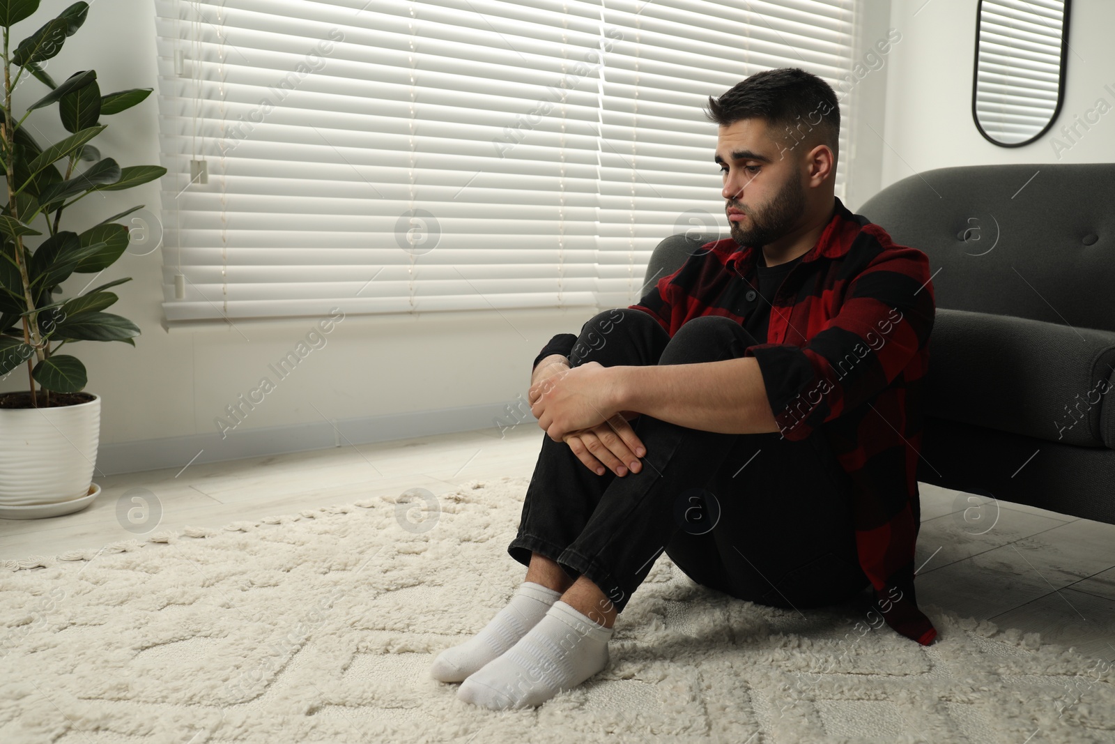 Photo of Sad man sitting on floor at home. Space for text