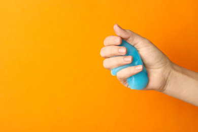 Photo of Woman playing with light blue slime on orange background, closeup. Antistress toy