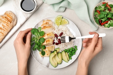 Photo of Woman eating boiled rice with vegetables and meat at table, top view