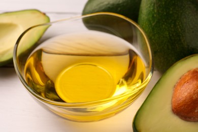 Photo of Cooking oil in bowl and fresh avocados on white wooden table, closeup