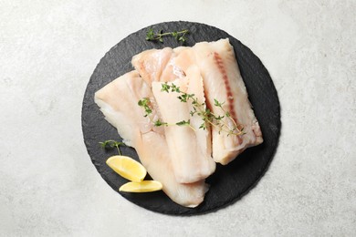 Photo of Pieces of raw cod fish and lemon on light grey table, top view