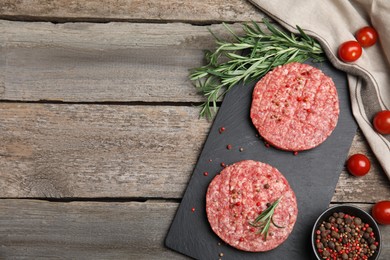 Photo of Raw hamburger patties with rosemary, tomatoes and peppercorns on wooden table, flat lay. Space for text