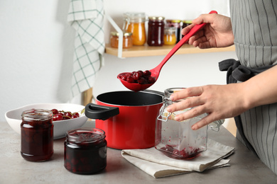 Photo of Woman making pickled cherries at table indoors, closeup