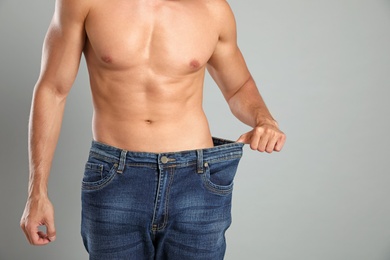 Young man with slim body in old big size jeans on grey background, closeup view. Space for text