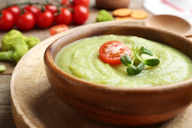 Photo of Bowl of broccoli cream soup with tomato and microgreens served on wooden tray, closeup