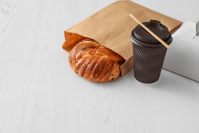 Photo of Paper bag with pastry and coffee on wooden table. Space for text