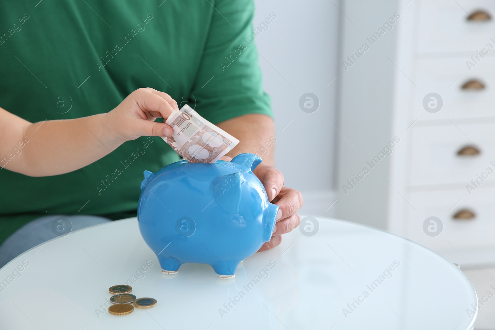 Photo of Little girl putting money into piggy bank and her grandfather at table, closeup. Space for text