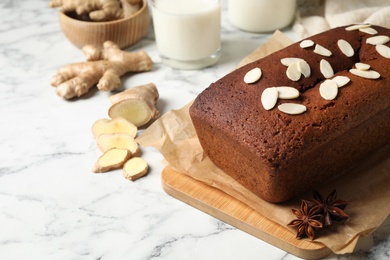 Photo of Delicious gingerbread cake with almond petals on white marble table