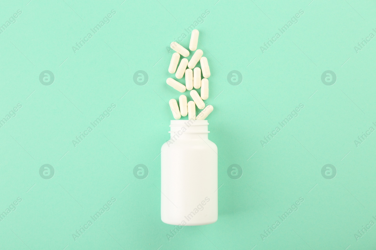 Photo of Bottle and vitamin capsules on turquoise background, top view. Space for text