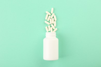 Bottle and vitamin capsules on turquoise background, top view. Space for text