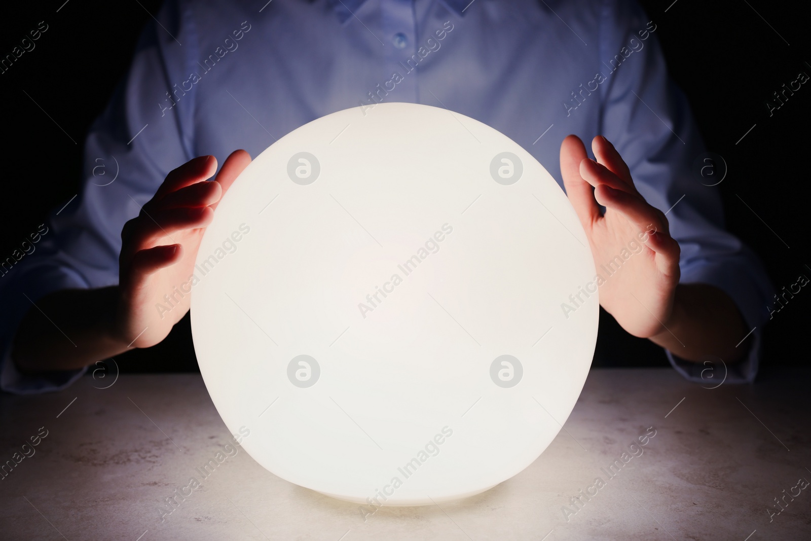 Photo of Businesswoman using glowing crystal ball to predict future at table in darkness, closeup. Fortune telling