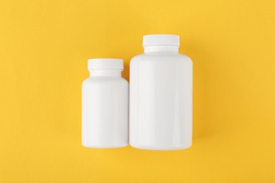 Photo of White medical bottles on yellow background, top view