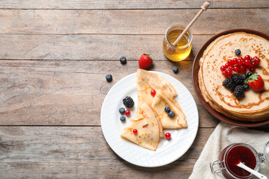 Photo of Delicious thin pancakes with berries on wooden table, flat lay. Space for text