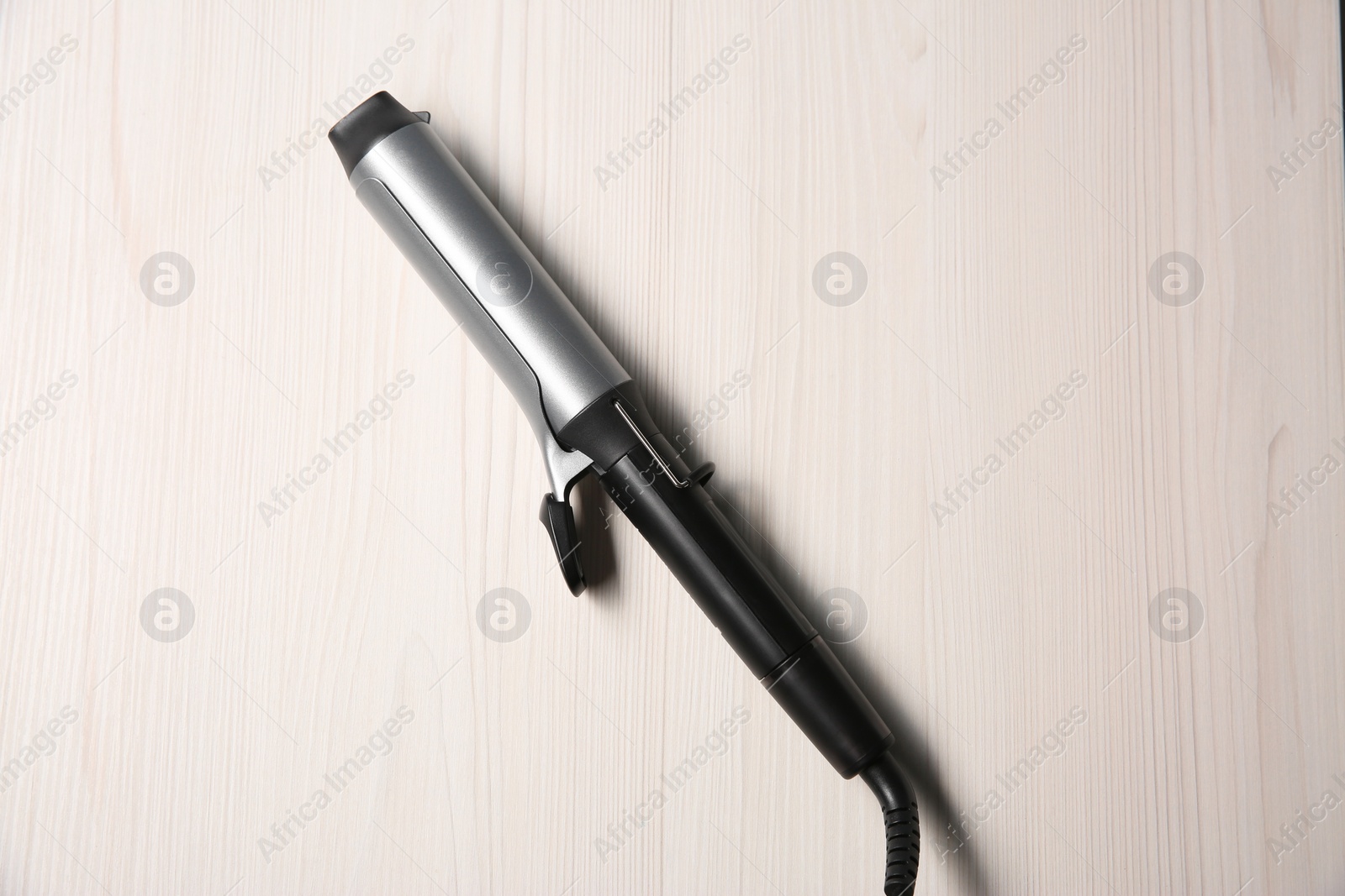 Photo of Hair curling iron on white wooden background, top view