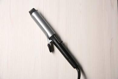 Hair curling iron on white wooden background, top view