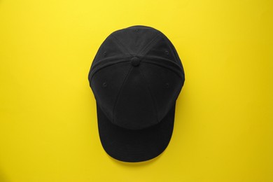 Photo of Stylish black baseball cap on yellow background, top view