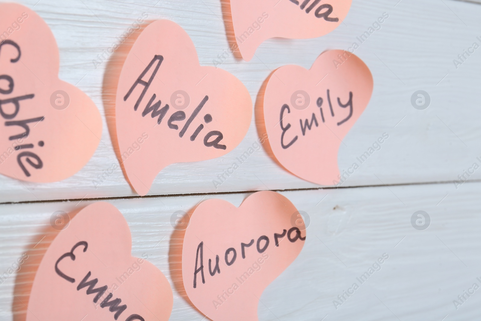 Photo of Paper stickers with different names on white wooden table, closeup. Choosing baby's name