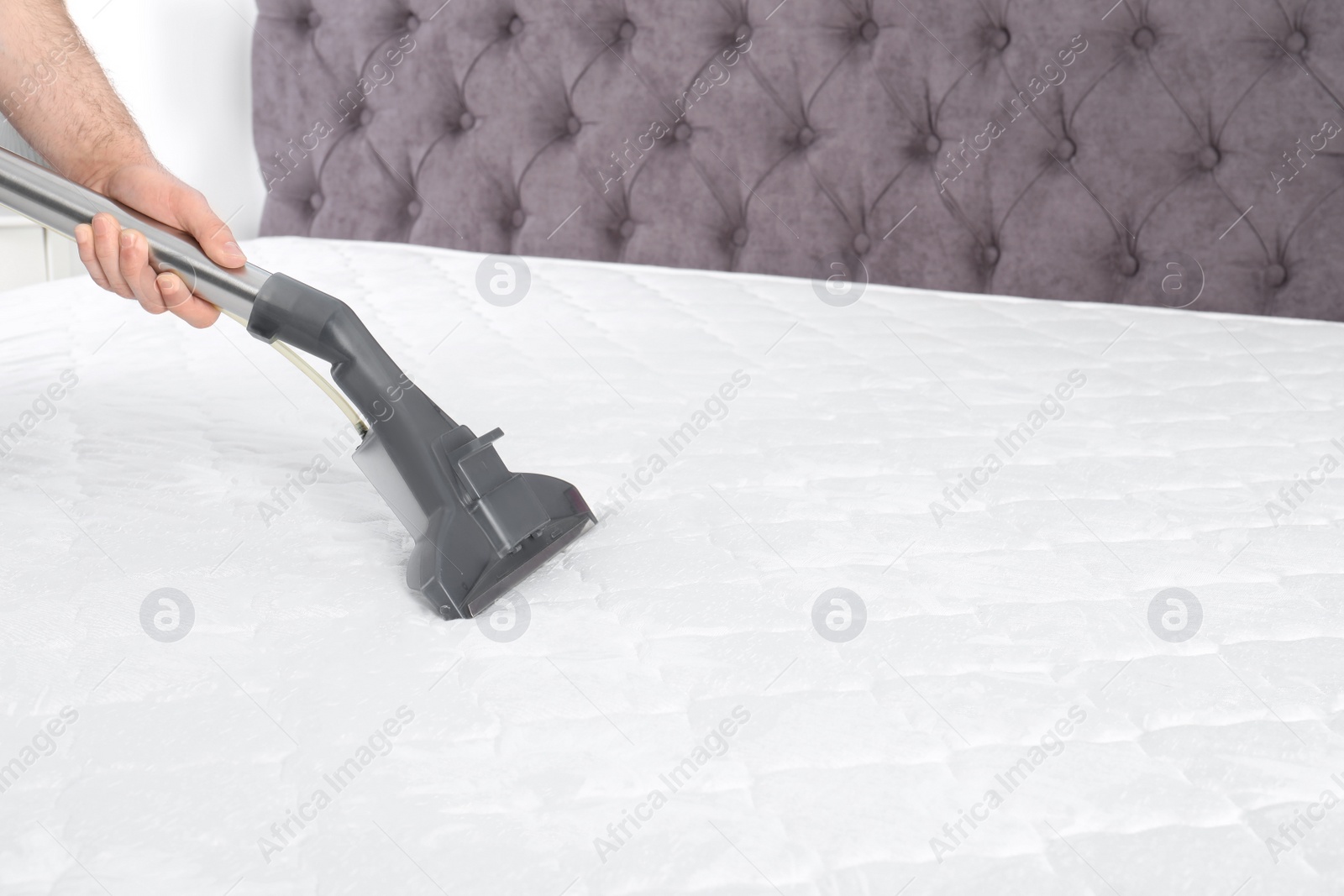 Photo of Man disinfecting mattress with vacuum cleaner, closeup. Space for text