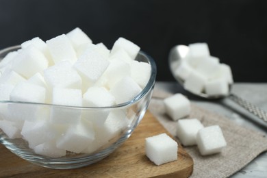 White sugar cubes in glass bowl on grey table, closeup