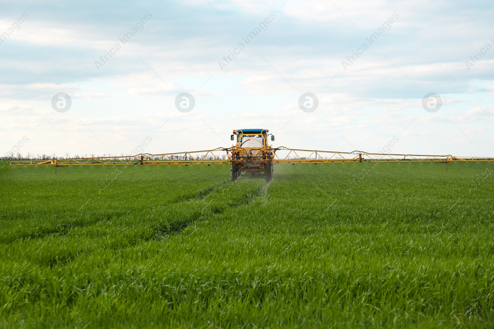 Photo of Tractor spraying pesticide in field on spring day. Agricultural industry