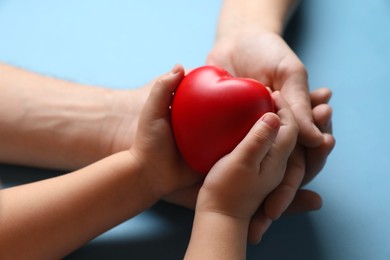 Photo of Father and his child holding red decorative heart on light blue background, closeup