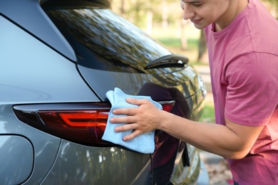 Young man washing car rear light with rag outdoors