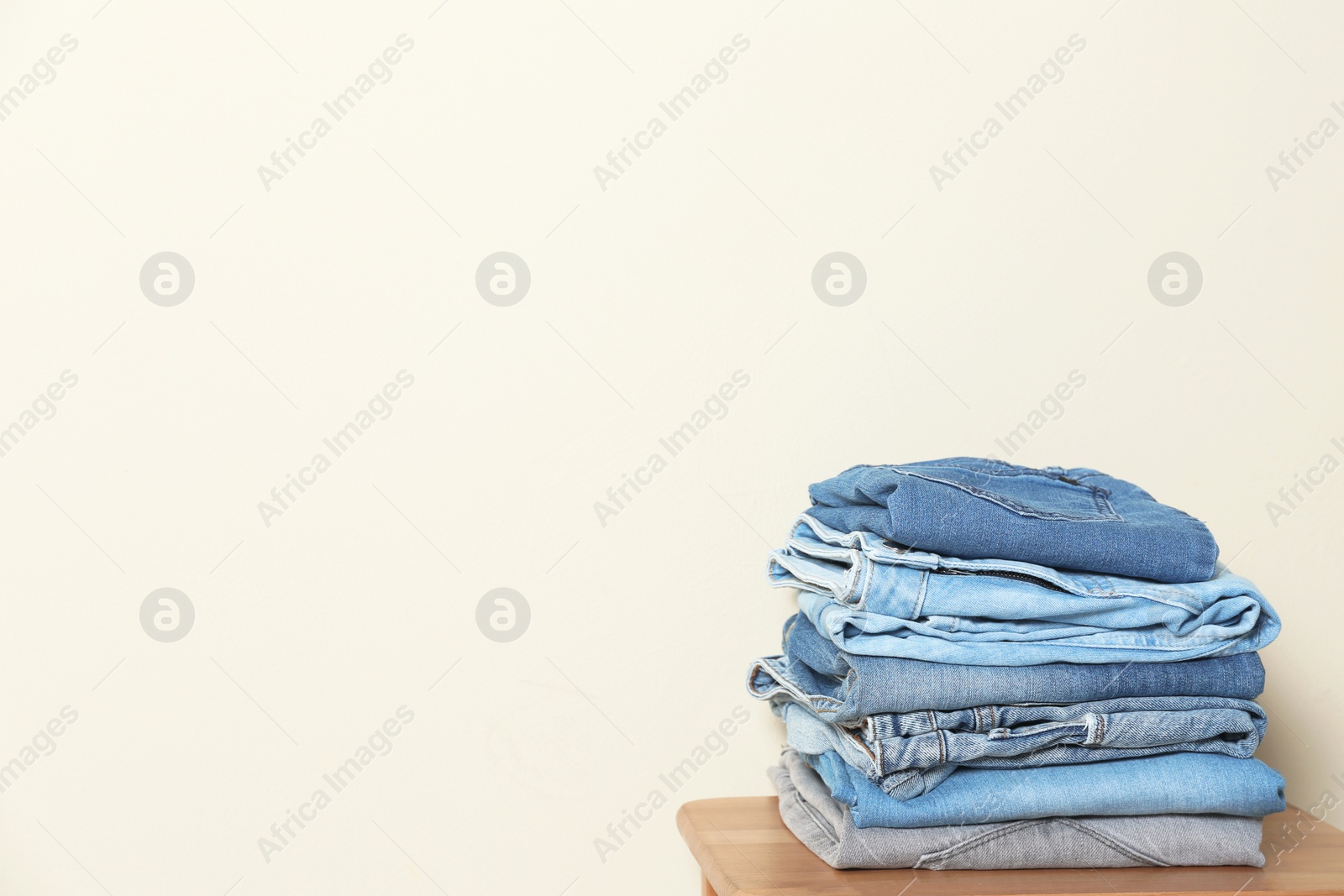 Photo of Stack of different jeans on table against light background. Space for text