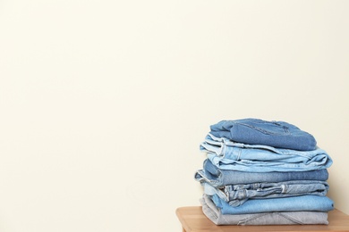 Photo of Stack of different jeans on table against light background. Space for text