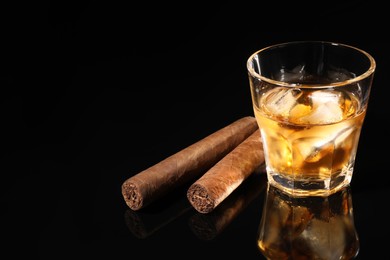 Photo of Glass of whiskey with ice cubes and cigars on black mirror surface. Space for text