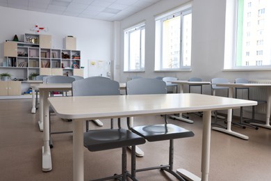 Photo of Empty school classroom with contemporary furniture and windows