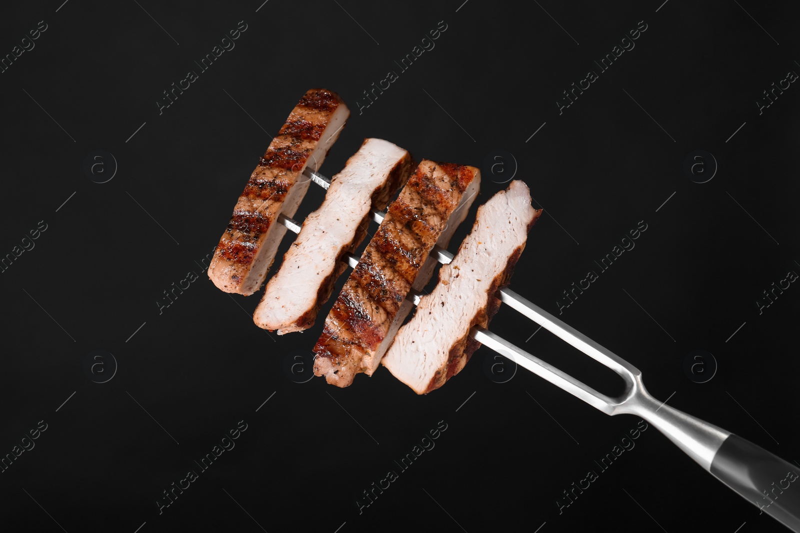 Photo of Carving fork with cut grilled pork steak pieces against black background