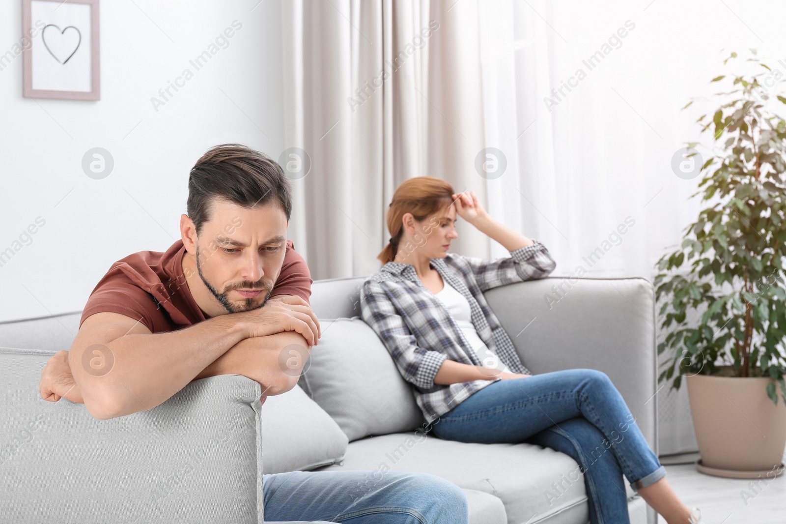 Photo of Couple ignoring each other after argument in living room. Relationship problems