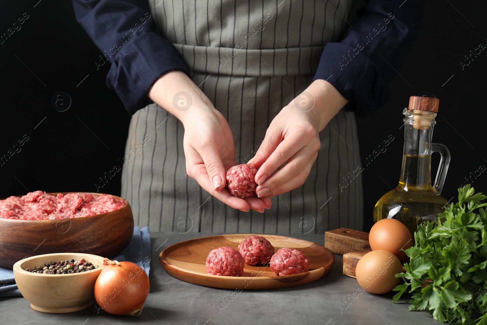 Photo of Woman making meatball from ground meat at grey table, closeup